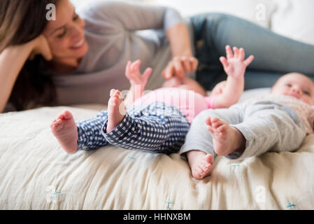 Madre caucasica giocando con twin baby figlie sul letto Foto Stock