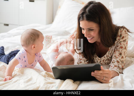 Madre caucasica sul letto con letti baby figlie con tavoletta digitale Foto Stock