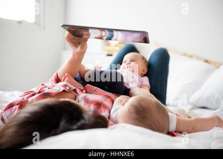 Madre caucasica sul letto con letti baby figlie con tavoletta digitale Foto Stock