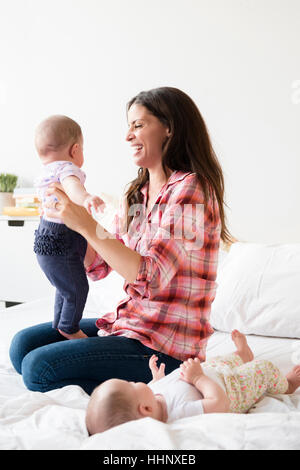 Madre caucasica giocando sul letto con letti baby figlie Foto Stock