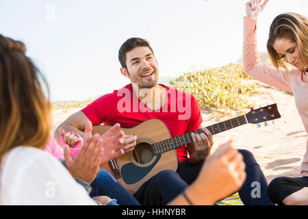 Uomo a suonare la chitarra per gli amici in spiaggia Foto Stock