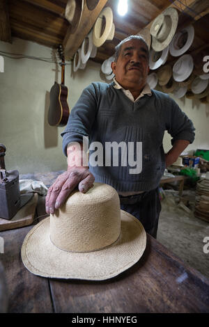 Luglio 22, 2016 San Bartolome, Ecuador: un cappello di paglia maker uomo appoggia la mano su una nuova hat Foto Stock