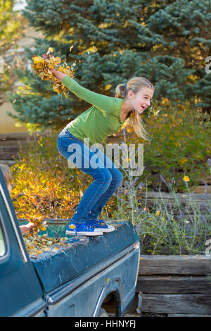 Caucasian ragazza con foglie di autunno jumping dal carrello Foto Stock