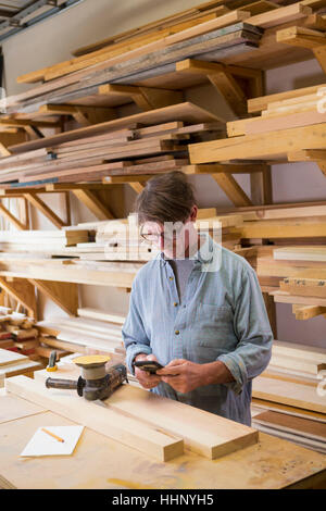 Falegname caucasica sms sul cellulare in officina Foto Stock