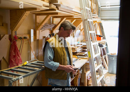 Falegname caucasica sms sul cellulare in officina Foto Stock