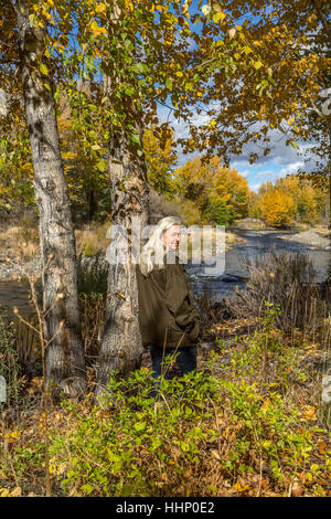 Sorridente donna caucasica appoggiata su albero vicino al fiume Foto Stock