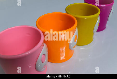 Tazze colorate su un bianco lucido tavolo. Foto Stock