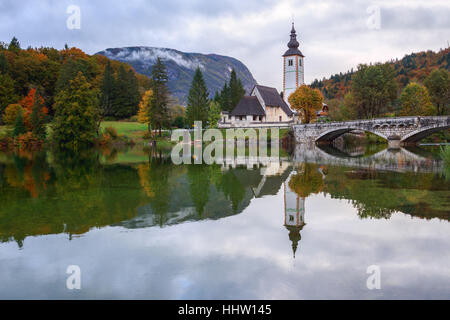 Il campanile della chiesa e il ponte di pietra sul lago di Bohinj nel villaggio alpino Ribicev Laz, Slovenia Foto Stock