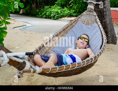 A dieci anni di vecchio ragazzo godendo di una amaca sulla bellissima isola tropicale della spiaggia di Koh Samui, Thailandia Foto Stock