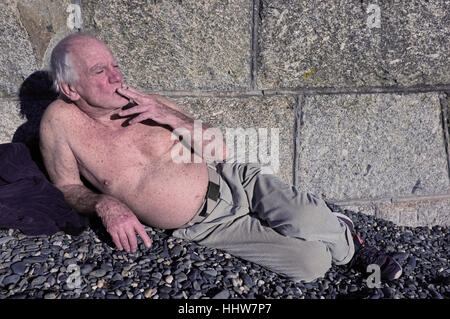Un vecchio uomo di fumare una sigaretta su una spiaggia in Penzance, Cornwall Foto Stock