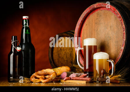 Natura morta con bottiglie di birra e bicchieri in una configurazione rustico con prezel, salsicce, grano e barili. Foto Stock