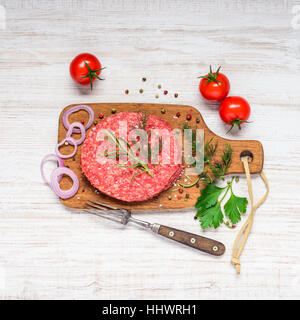 Materie e sminuzzato Burger di carne con spezie, cucina erbe e verdure sul tagliere di legno Foto Stock