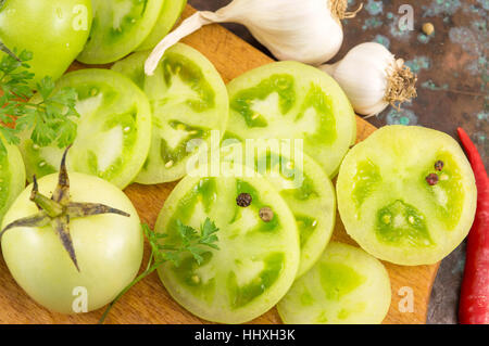 Fette di pomodoro verde con aglio e peperoni rossi su un tagliere di legno Foto Stock