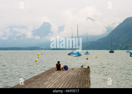 ST. GILGEN, Austria - luglio5, 2013: un paio di relax su un molo in legno sul lago Wolfgangsee nelle Alpi austriache. Foto Stock