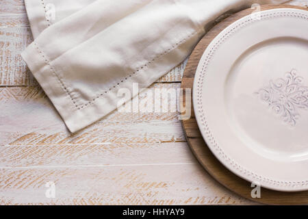 White vintage piastra vuota sul round tagliere, panno di lino bianco su uno sfondo di legno, stile provenzale, cucina interno Foto Stock