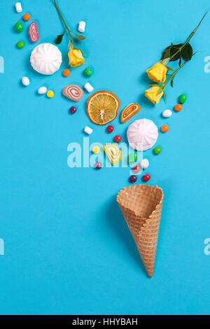 Marshmallows, candy, Jelly Beans, dolci , tazze secchi Arance e giallo rose rientranti nel cono di wafer su uno sfondo blu. Spazio di copia Foto Stock