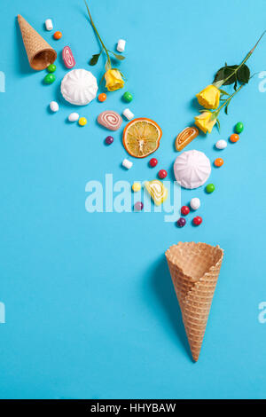 Marshmallows, candy, Jelly Beans, dolci , tazze secchi Arance e giallo rose rientranti nel cono di wafer su uno sfondo blu. Spazio di copia Foto Stock