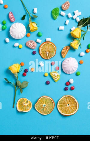 Marshmallows, candy, Jelly Beans, dolci , tazze secchi Arance e giallo rose rientranti nel cono di wafer su uno sfondo blu. Spazio di copia Foto Stock