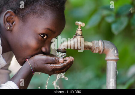 Bellissimo bambino africano di bere da un rubinetto (acqua scarsità simbolo). Giovane ragazza africana di bere acqua pulita da un rubinetto. Versare acqua da un rubinetto in t Foto Stock