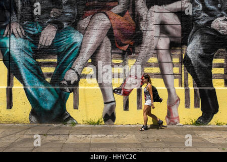 Una donna cammina passato una città murale raffigurante seduta coppie, città di Buenos Aires, Argentina. Foto Stock