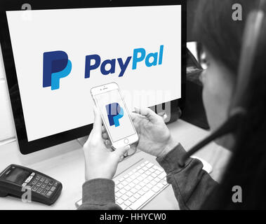 Membro del personale utilizzando il sito Web di PayPal e lo smartphone app per fornire i clienti con supporto Foto Stock