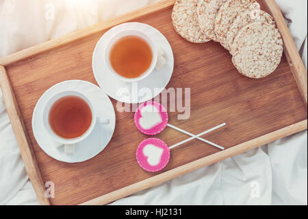 La prima colazione a letto nel giorno di San Valentino. Tazza di tè e dolci caramelle. Amore o il concetto di vacanza. Foto Stock