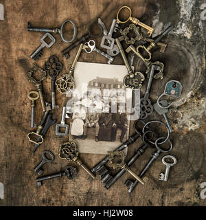 Vintage foto ritratto di famiglia con casa sullo sfondo. Vecchie chiavi su texture di legno Foto Stock