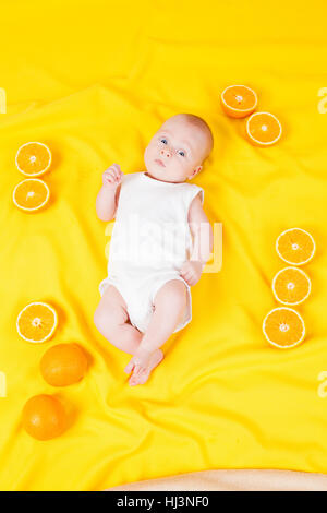 Baby boy giace su un giallo con arance Foto Stock
