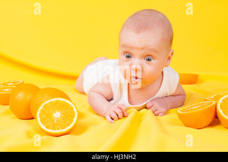 Baby boy giace su un giallo con arance Foto Stock