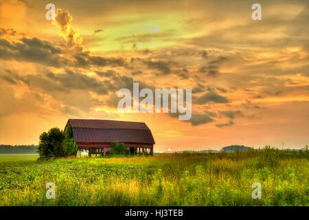Fienile in legno del tramonto. Tramonto rurale con un fienile abbandonato circondato da campi di fattoria. Foto Stock