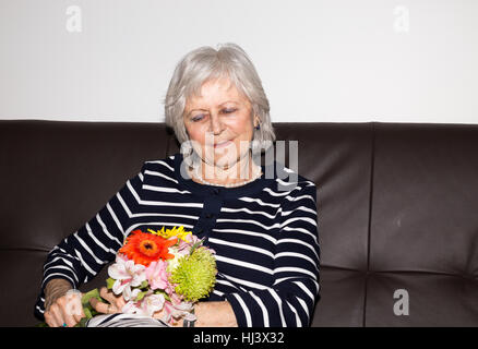 Senior bella donna seduta e tenendo i fiori. Foto Stock