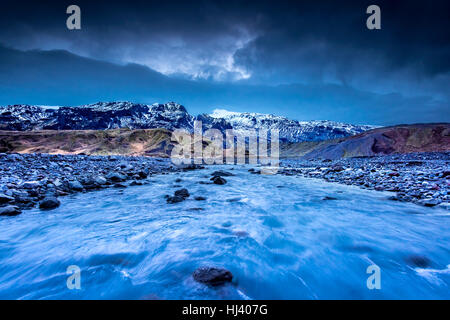 Un fiume formata mediante fusione dei ghiacciai fluisce attraverso una gamma di montagna nel nord dell'Islanda durante un buio, giorno piovoso. Foto Stock
