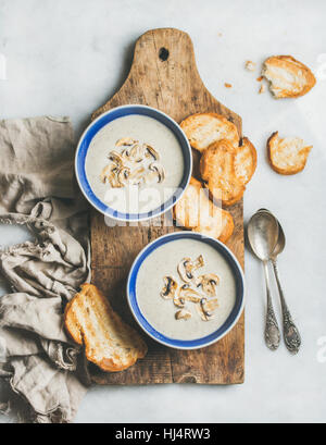 Cremosa zuppa di funghi in ciotole con pane tostato, Sfondo marmo Foto Stock