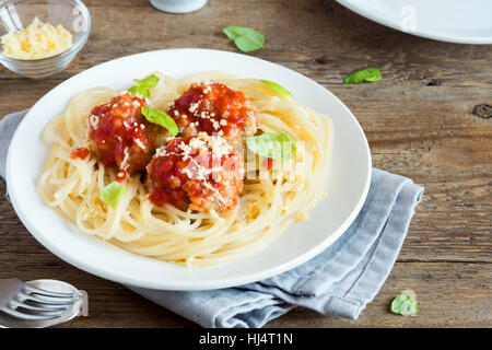 Gli spaghetti con le polpette di carne, salsa di pomodoro, formaggio parmigiano grattugiato e basilico fresco - una sana casalingo italiano sulla pasta di legno rustico sfondo con Foto Stock