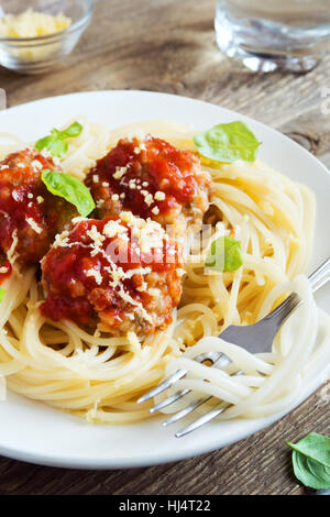 Gli spaghetti con le polpette di carne, salsa di pomodoro, formaggio parmigiano grattugiato e basilico fresco - una sana casalingo italiano sulla pasta di legno rustico sfondo con Foto Stock