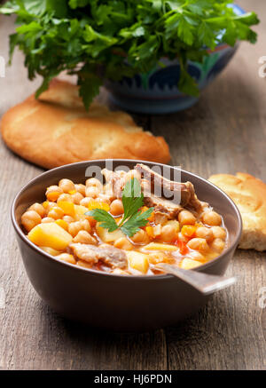 Zuppa di agnello i ceci in una terrina, il prezzemolo e il pane piatto sul vecchio sfondo di legno Foto Stock