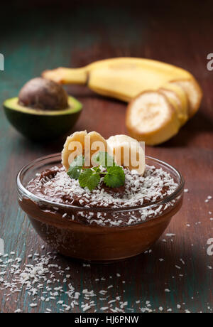 Materie vegane avocado budino di banana con briciole di noce di cocco in una ciotola di vetro Foto Stock