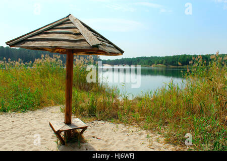 Ombrello in legno sulla sabbia vicino al bellissimo lago nella foresta Foto Stock