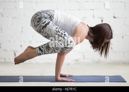 Giovane donna attraente in Bakasana pongono, bianco di sfondo per studio Foto Stock