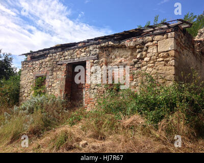 La rovina di cottage in pietra con ricoperta di vegetazione sulla cima della montagna nel nord Italia Foto Stock