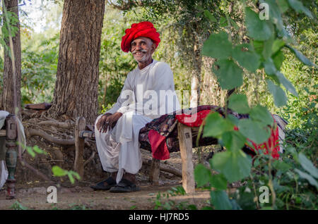 Senior di Rajasthani uomo seduto su khaat nella sua fattoria. Foto Stock