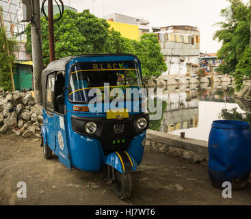 Triciclo blu in Indonesia noto come Bajaj parcheggiata accanto al fiume sporco in baraccopoli zona foto scattata a Giacarta Foto Stock