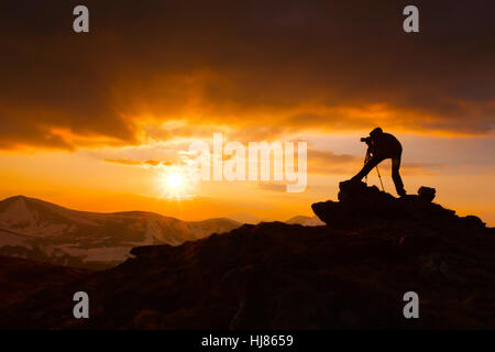 Silhouette di un fotografo che spara un tramonto in montagna Foto Stock