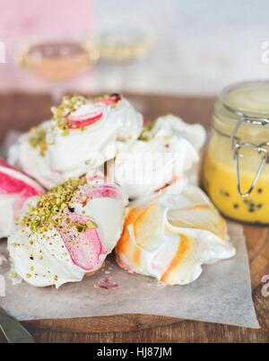 Pistacchio colorato meringhe impilati su una breadboard e la carta da forno con granadiglie & cagliata di limone in un barattolo di vetro. Foto Stock