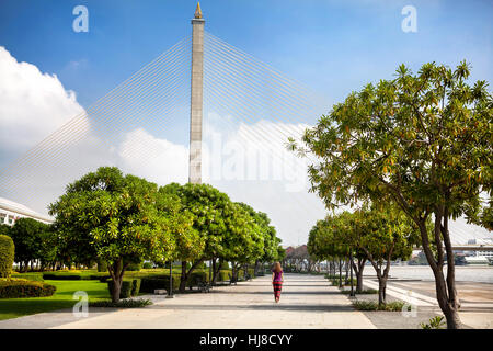 Donna che cammina nel parco vicino al Ponte di Rama VII a Bangkok, in Thailandia Foto Stock