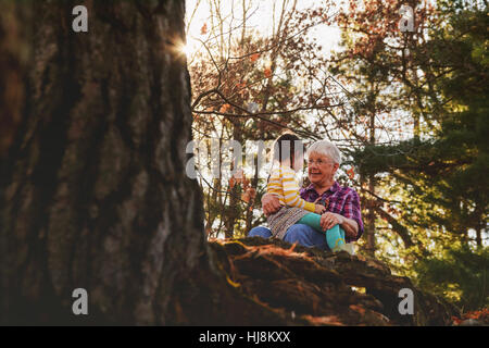 Nonna e nipote seduta nella foresta di parlare Foto Stock