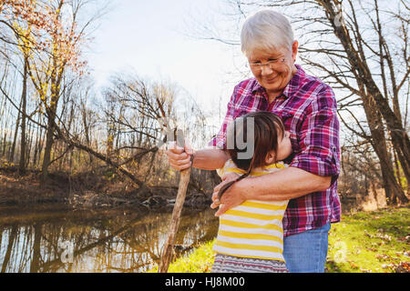 Ragazza abbracciando la nonna nella foresta da un fiume Foto Stock
