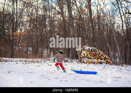 Ragazzo tirando la sua slitta attraverso la neve passato un palo di legno Foto Stock