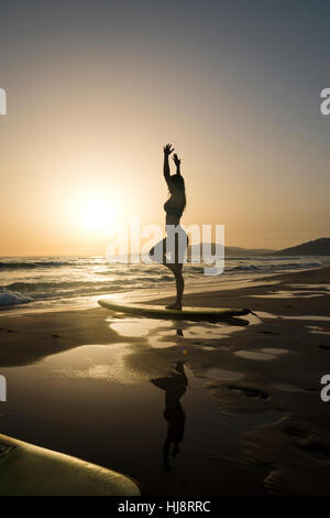 Silhouette di donna fare yoga su una tavola da surf, spiaggia los Lances Tarifa, Cadice, Andalusia, Spagna Foto Stock