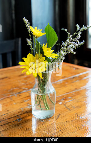 Bocciolo di vetro vaso con Giallo e Bianco Fiori su una tavola in legno rustico, alla luce del sole in streaming attraverso la finestra Foto Stock